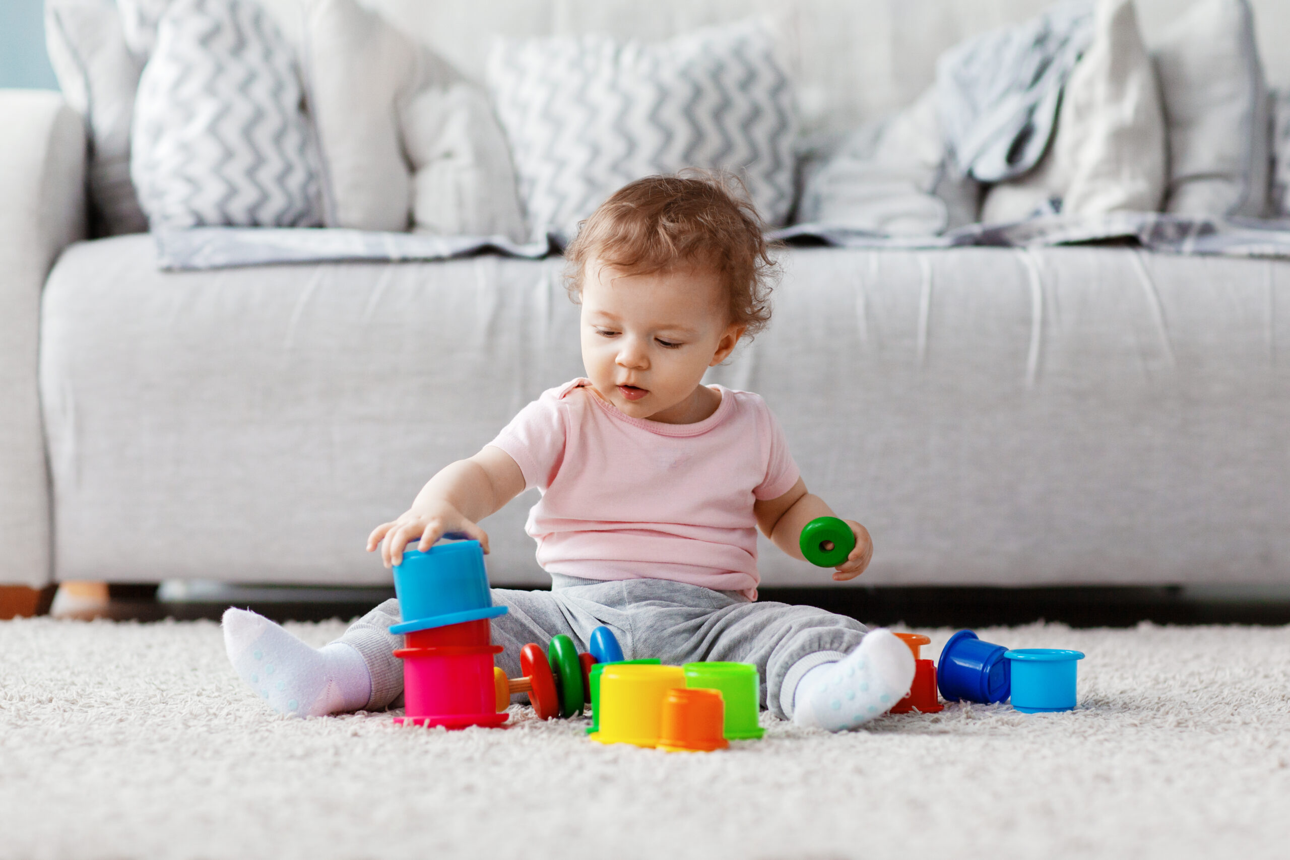 The kid plays on the floor on a light carpet with bright toys, builds a tower